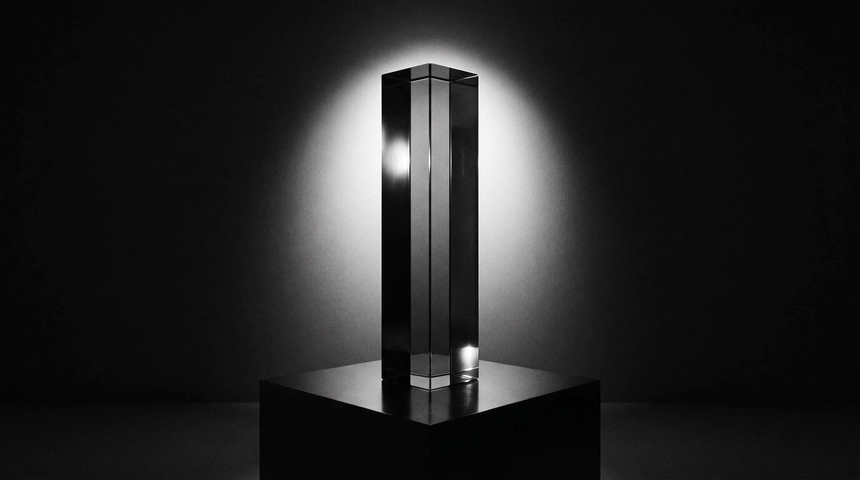 A tall glass monolith trophy on a black plinth, backlit so its edges glow against the dark.